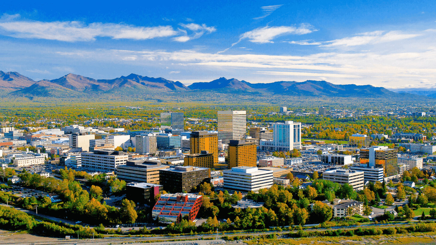 A panoramic sightseeing view of a city skyline with modern buildings set against a backdrop of mountains and clear skies.