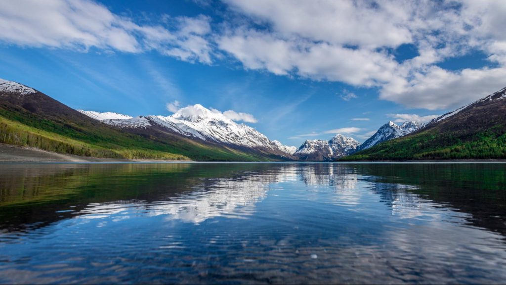 Snow-capped mountains and green forests overlooking Eklutna Lake in Alaska.