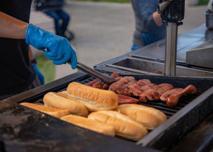 Person grilling hot dogs and toasting buns at an outdoor event during a Guided Anchorage Food Tour.