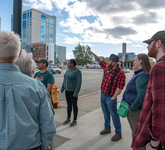 Group of people on an Anchorage sightseeing walking tour with a guide pointing out a feature.