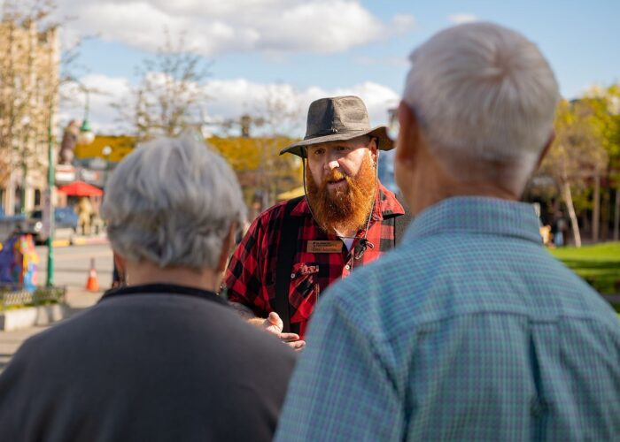 Man with a beard wearing a hat having a conversation with two other individuals outdoors during a Guided Anchorage Food Tour.