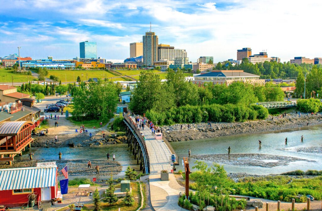 A vibrant view of a cityscape with a pedestrian bridge crossing over a river, flanked by greenery and urban buildings under a clear sky, perfect for sightseeing.