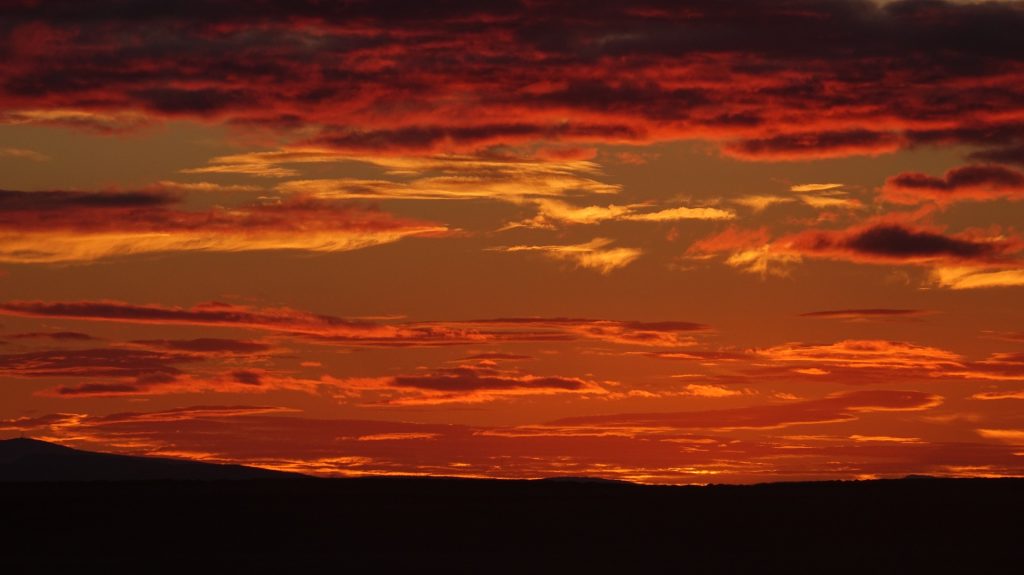 Vibrant sunset with orange and red clouds over a silhouette of a mountainous horizon.