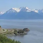 A scenic coastal road curves along the shoreline with mountain peaks in the background, partially covered in snow under a clear sky—a signature view of unique Alaska and one of the classic Anchorage experiences. A scenic coastal road curves along the shoreline with mountain peaks in the background, partially covered in snow under a clear sky—a signature view of unique Alaska and one of the classic Anchorage experiences.